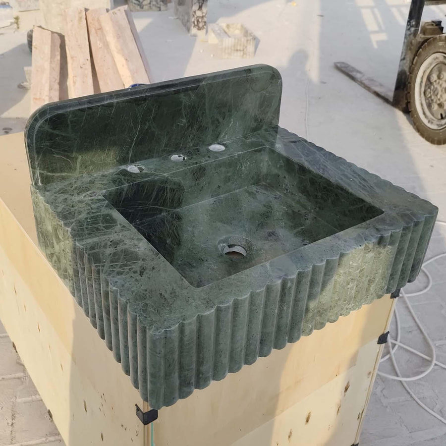 Hand-carved green marble console sink with rounded backsplash and widespread brass faucet in a bathroom