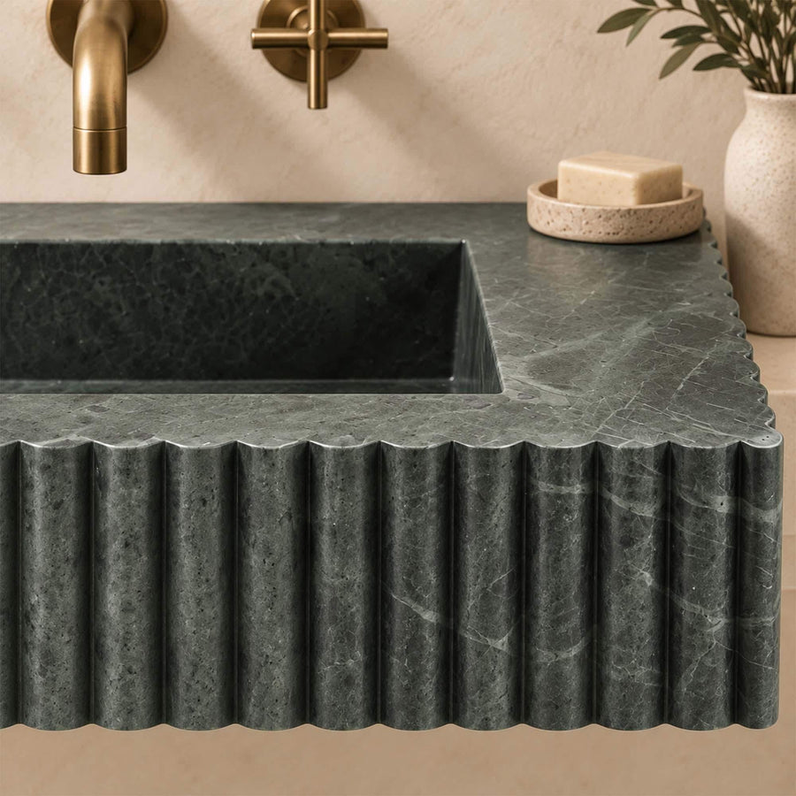 Fluted green marble console basin with natural light veining on a plaster wall