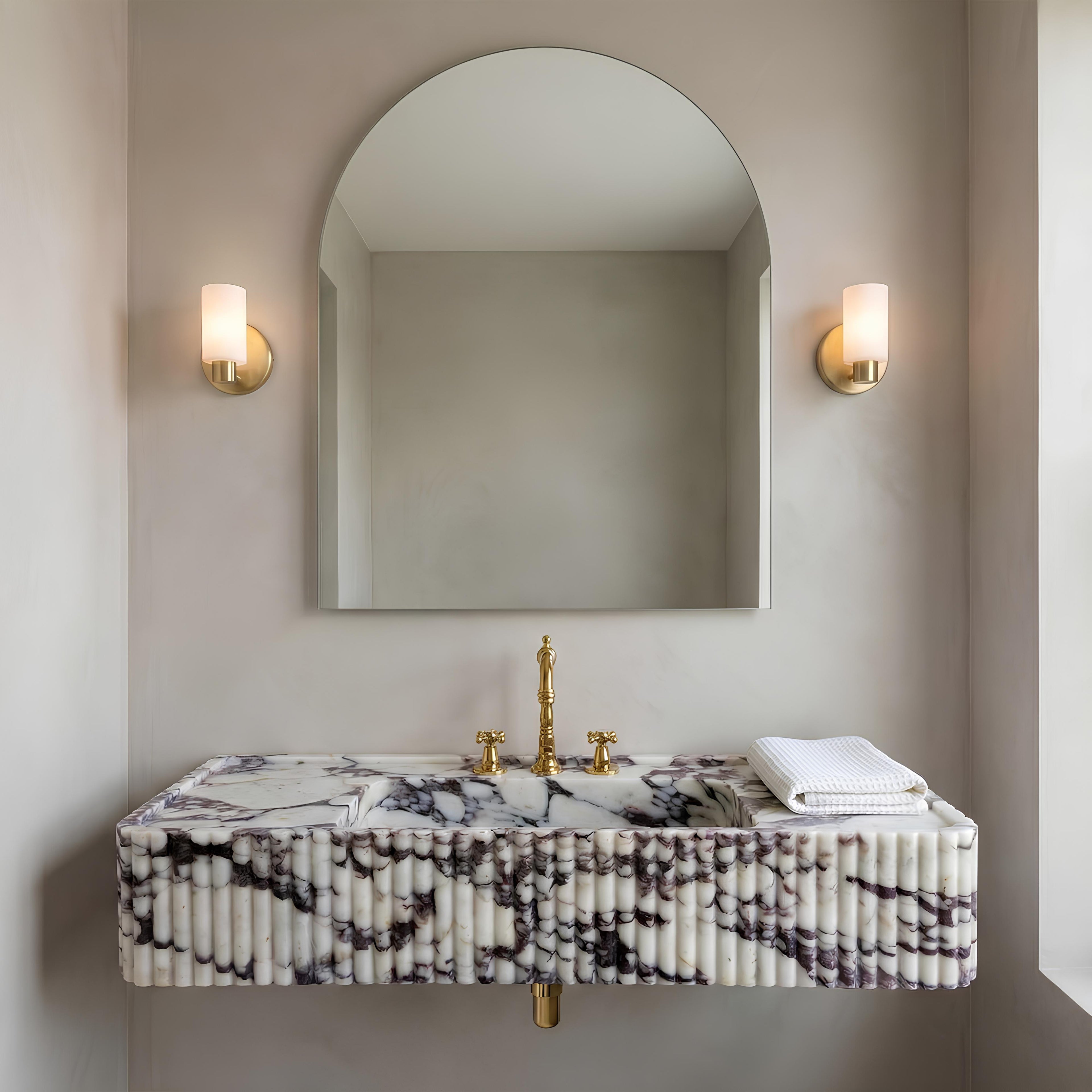 Bathroom vanity with marble countertop, gold fixtures, and wall-mounted mirror.