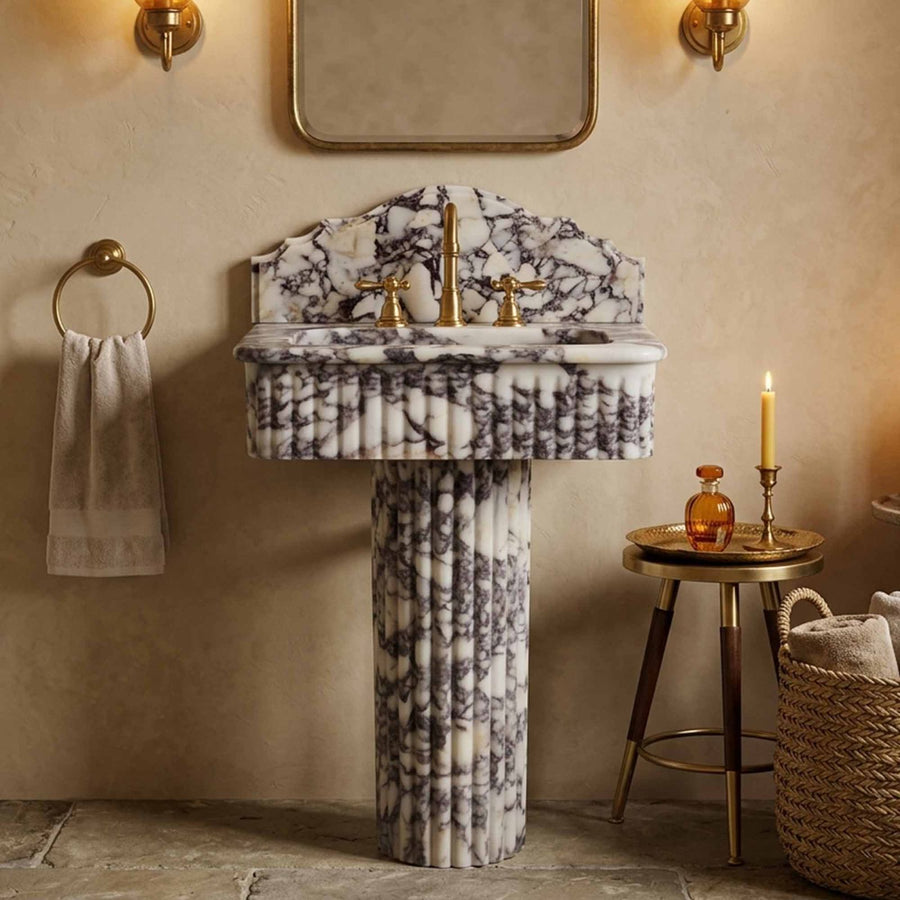 Marble pedestal sink with scalloped backsplash and brass fixtures