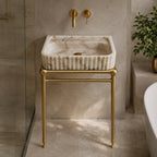 Calacatta Gold marble sink on brass console legs next to a glass shower