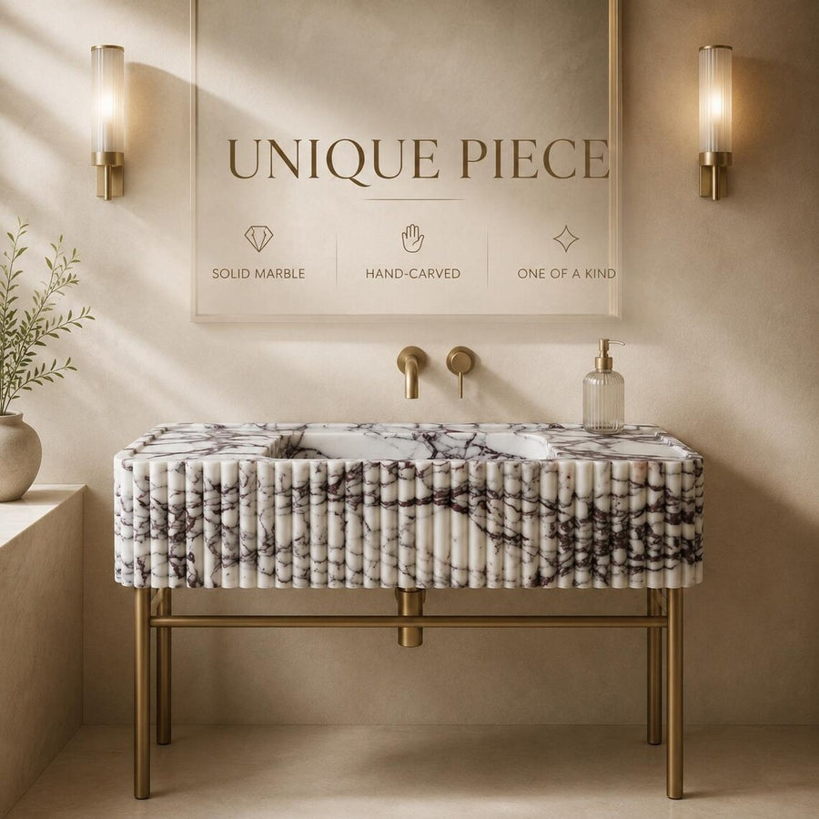 A luxury bathroom vanity featuring a fluted marble sink top with black and white veining, supported by a ribbed gold metal frame. The vanity is styled in a warm, elegant bathroom setting with a matching marble-look wall mirror, gold wall sconces, and brass faucet fixtures.