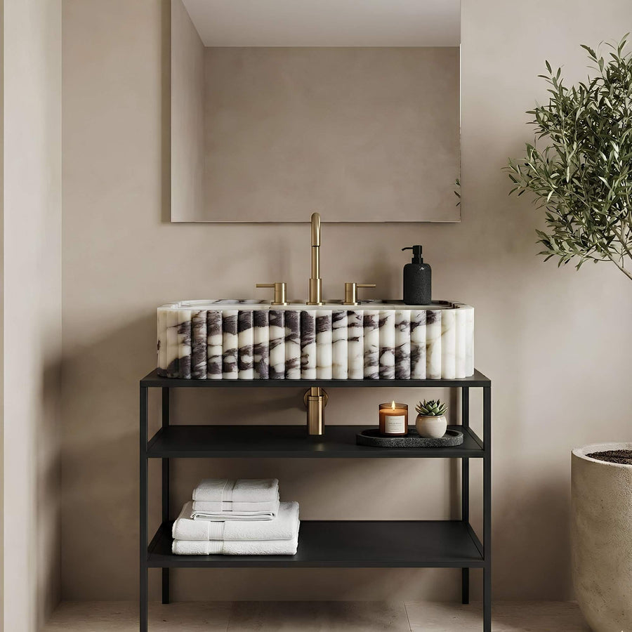 Bathroom vanity with marble countertop, black shelves, and decorative items against a beige wall.