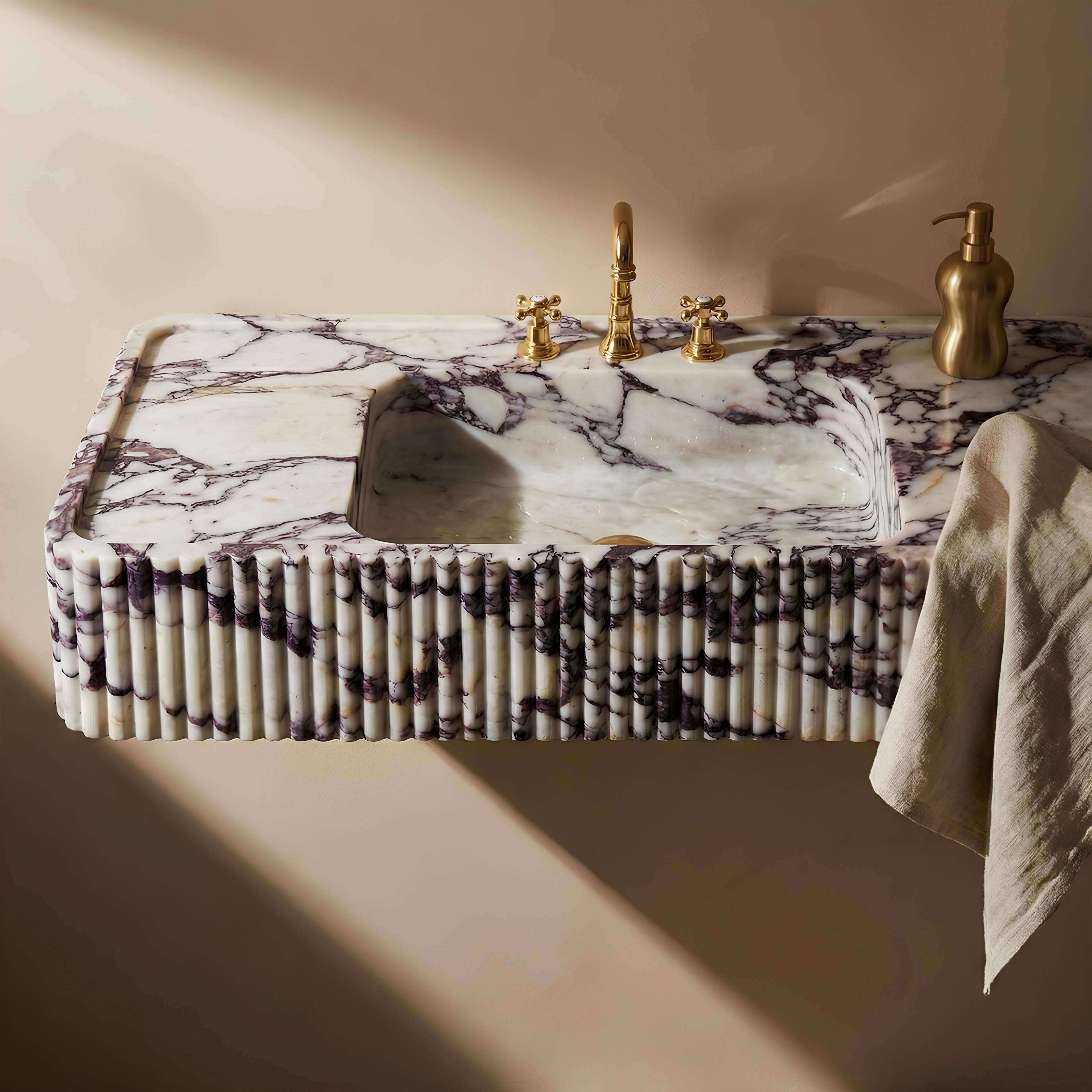 Marble-patterned sink with gold fixtures on a beige wall.