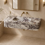 A floating rectangular bathroom sink with a white marble-look surface and dark veining, mounted against a beige wall with a gold-framed mirror, brass faucet, and sconces.