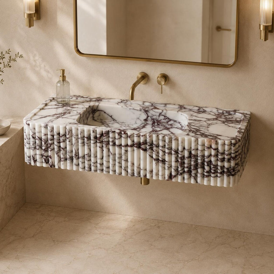 A floating rectangular bathroom sink with a white marble-look surface and dark veining, mounted against a beige wall with a gold-framed mirror, brass faucet, and sconces.