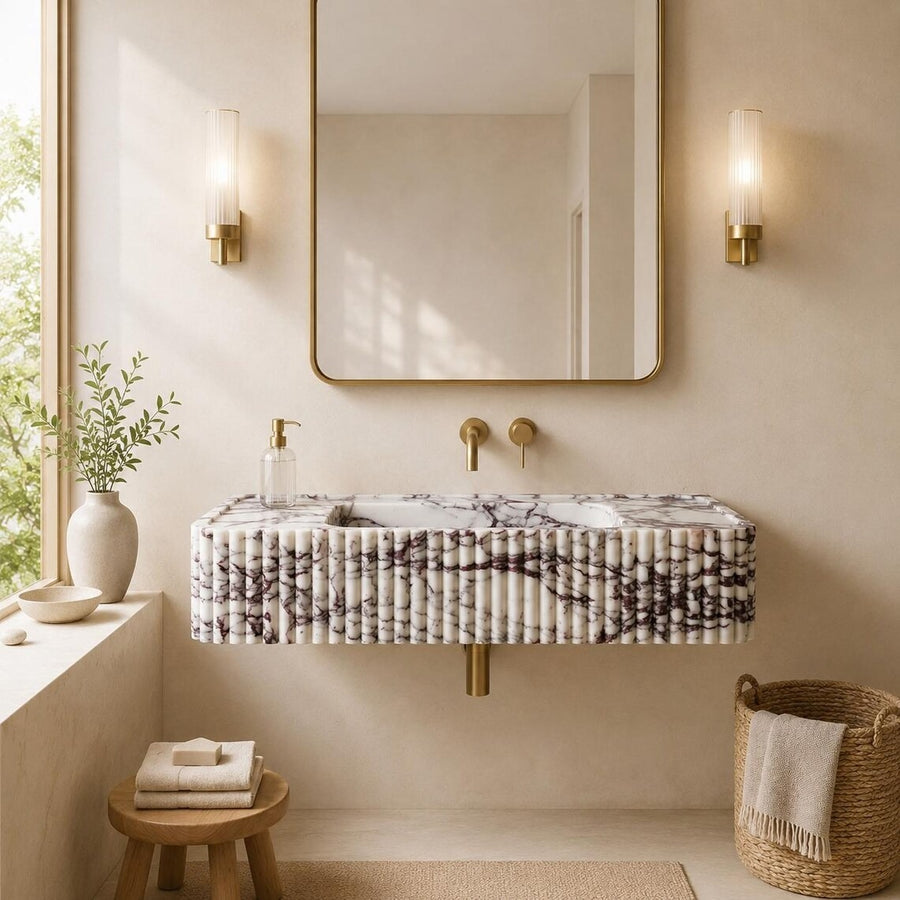 A modern floating bathroom vanity with a ribbed white marble-look front, gold faucet hardware, a large rectangular mirror, and two warm wall sconces in a softly styled bathroom setting.