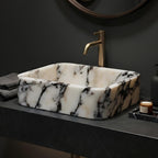 Bathroom vanity with marble sink and gold faucet against a dark wall.