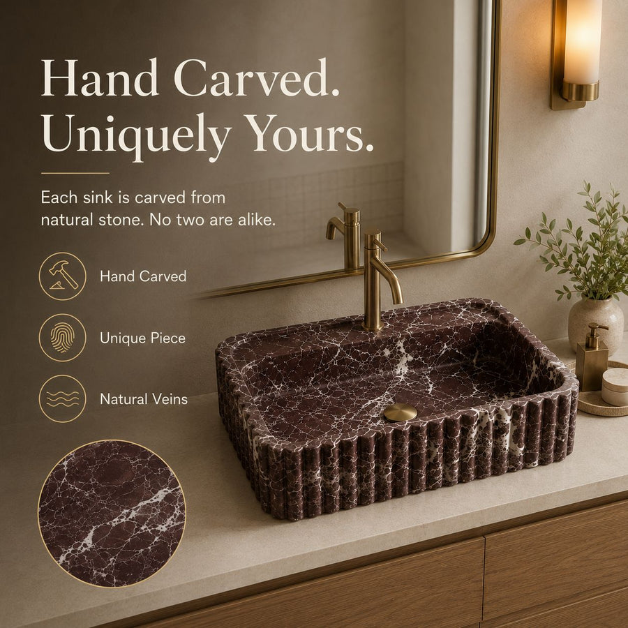 A hand-carved rectangular stone bathroom sink with a ribbed front edge and a brass faucet, shown installed on a vanity in a styled bathroom setting. Text on the left highlights 'Hand Carved.