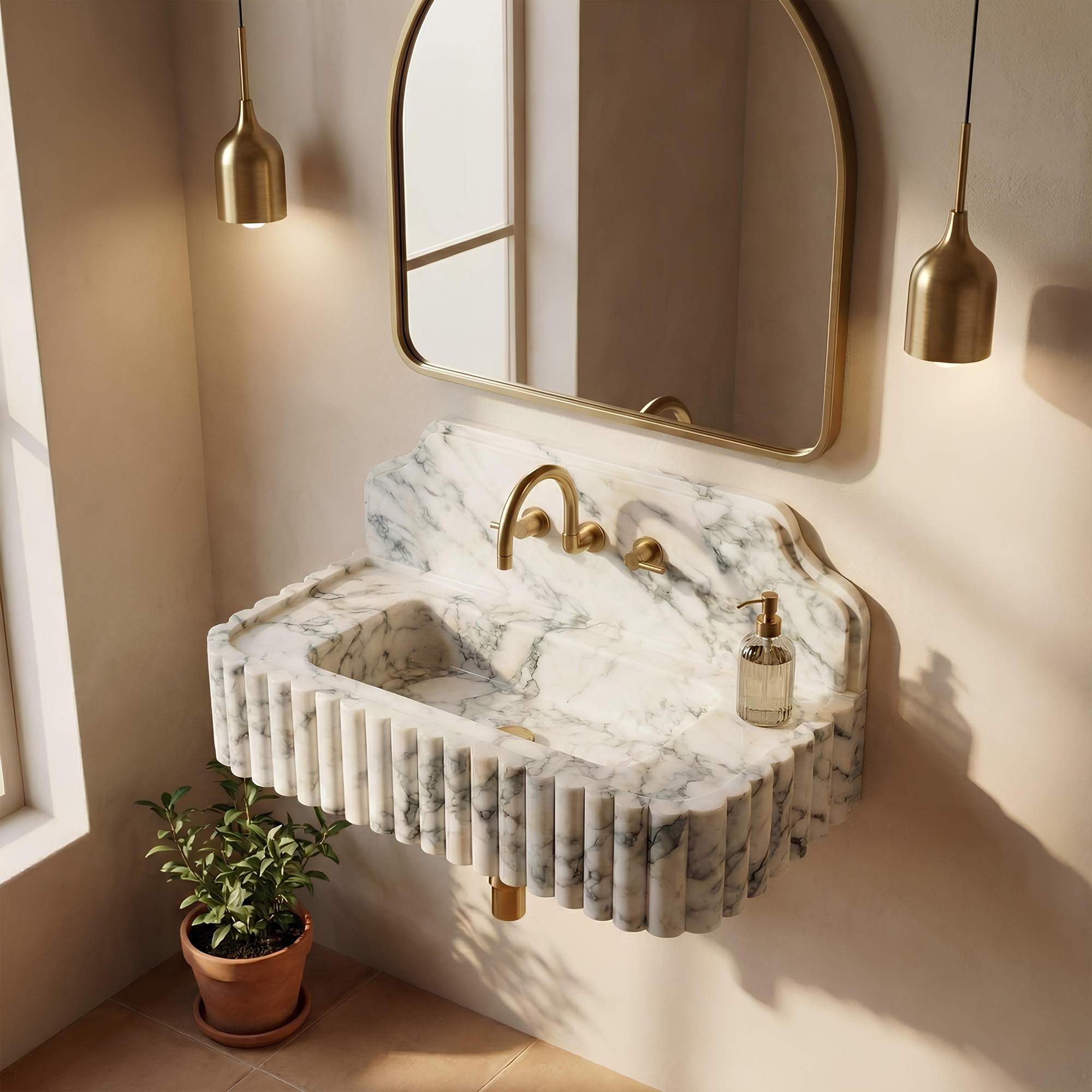 A floating marble sink with fluted edges and a curved backsplash, paired with a gold faucet and gold-framed wall mirror, shown in a styled bathroom setting with warm sunlight and a small potted plant.