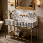 A luxury bathroom vanity featuring a ribbed white and gray marble sink basin on a polished gold metal frame, styled with a gold faucet, gold wall sconces, and a gold mirror in a warm, elegant room.