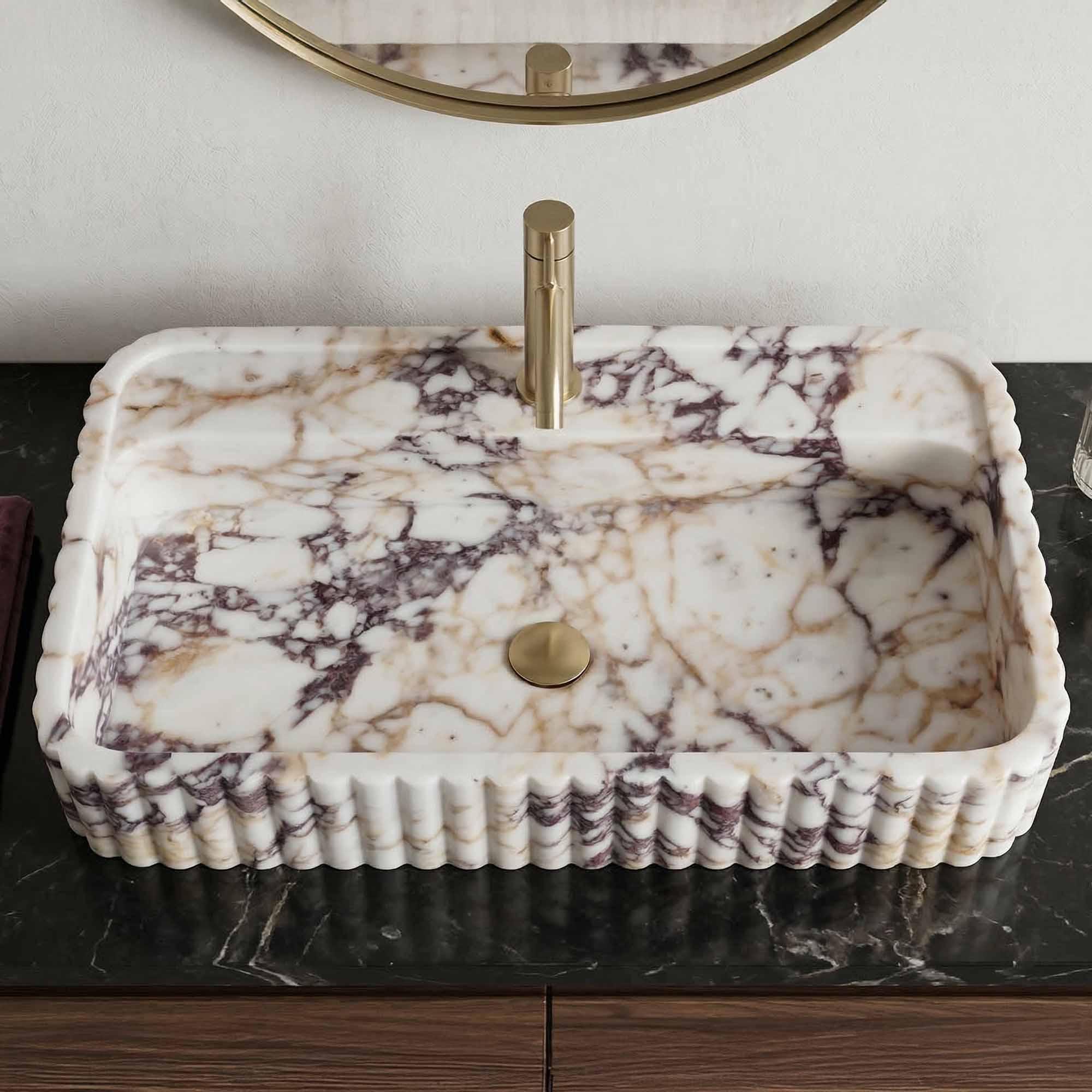 Marble-patterned rectangular sink with gold faucet on a dark countertop.