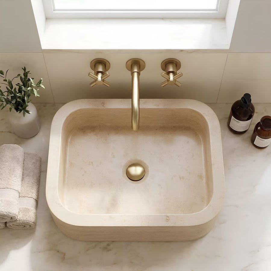 Top view of travertine stone sink with brass faucet on marble countertop