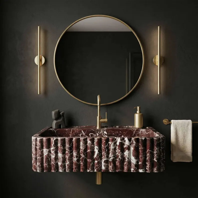 Bathroom vanity with marbled sink, round mirror, and gold fixtures on a dark wall.