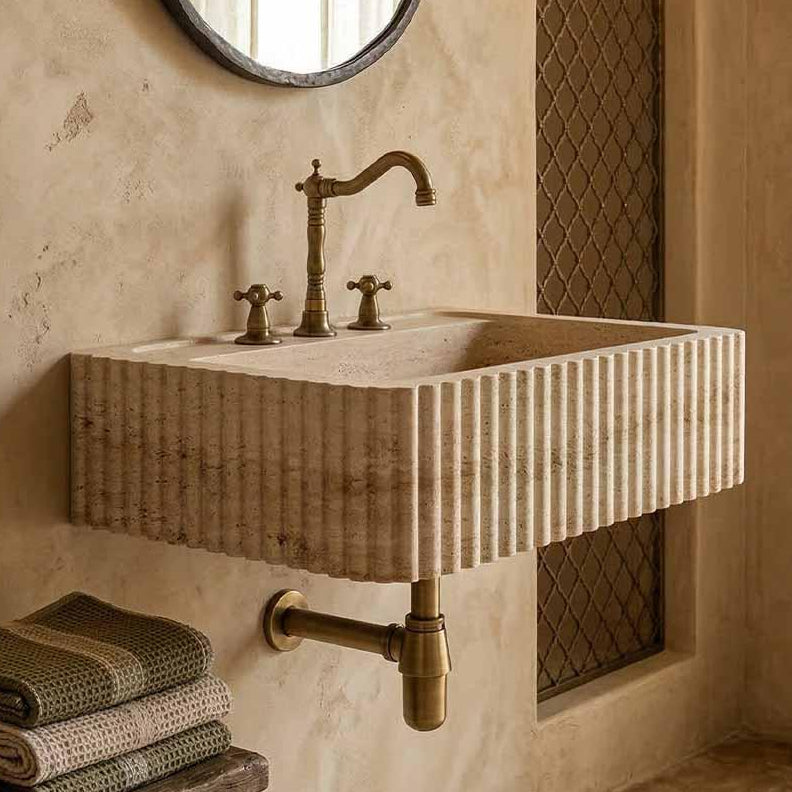 Beige stone sink with bronze faucet in a rustic bathroom setting