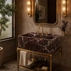A luxury bathroom vanity featuring a rectangular marble sink with dark reddish-brown and white veining, mounted on a polished gold brass stand. The setup includes a matching gold faucet, gold wall sconces, a large decorative mirror, and a small shelf holding folded towels and toiletries, all set against a textured warm brown wall.